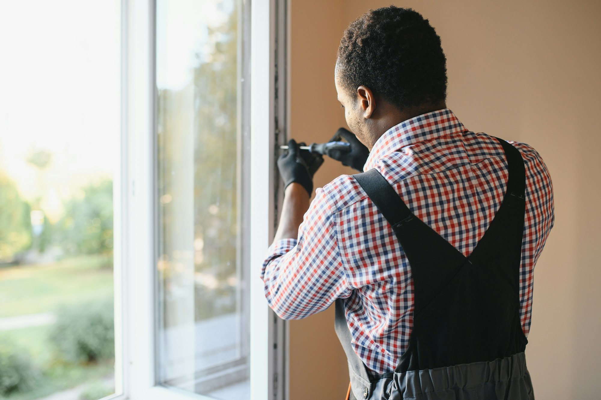 Close-up Of Young African Handyman In Uniform Installing Window