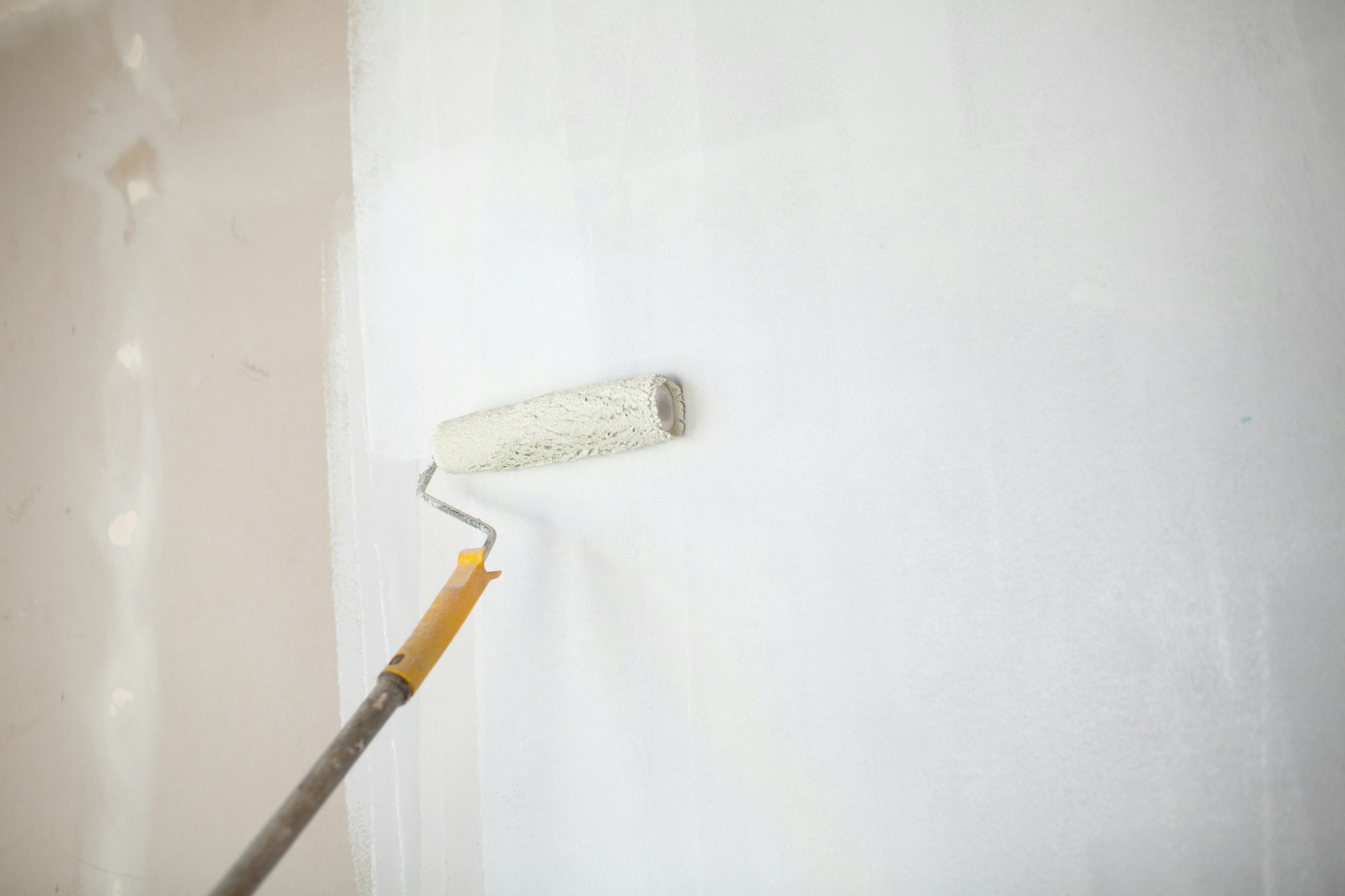 White paint roller in hand with drywall wall painting